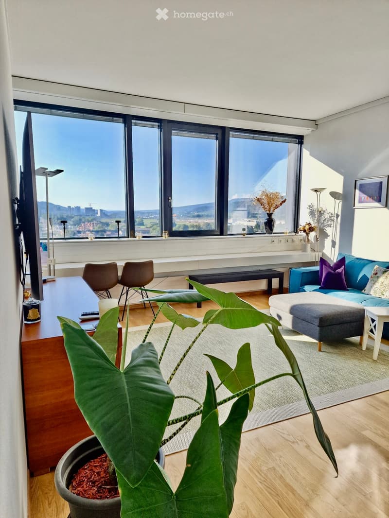 large windows, wooden floor, beige rug, blue sofa, coffee table, armchairs, TV, potted plant, desk, remote control, lamp