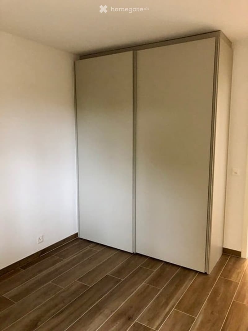 Empty room with white walls, wooden floor, and a double sliding wardrobe