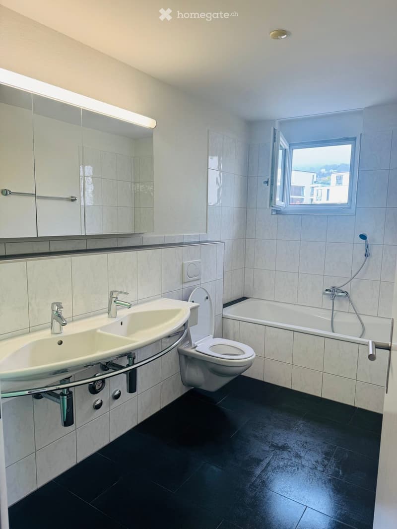 Bathroom with white tiles, black floor, double sink, toilet, bathtub, mirror, window