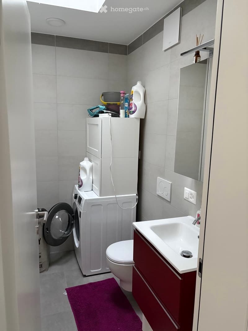 modern bathroom with white tiles, white washing machine, dryer, sink, toilet, mirror, and shelves