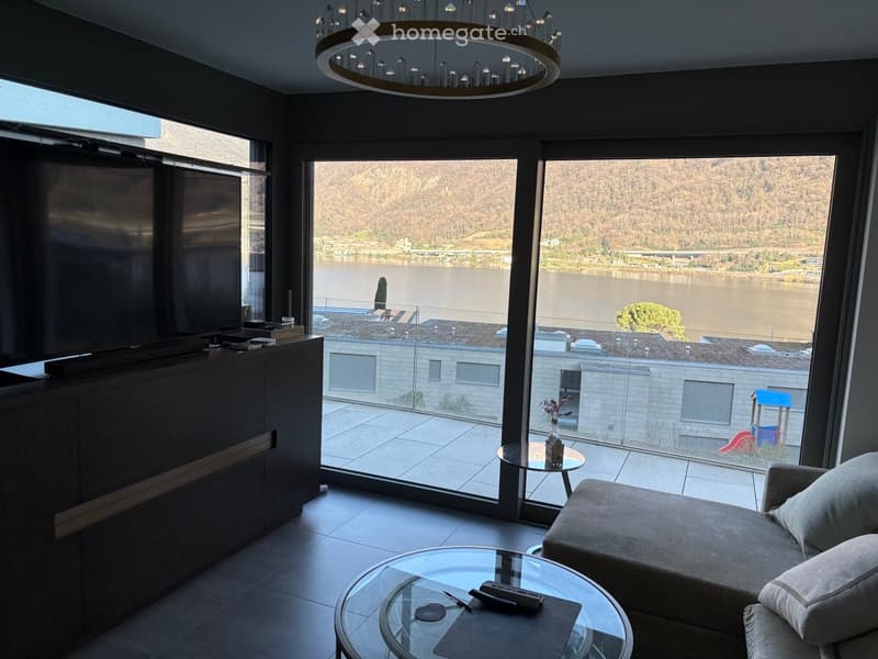 large windows, couch, coffee table, TV, entertainment center, chandelier, glass table, view of the lake