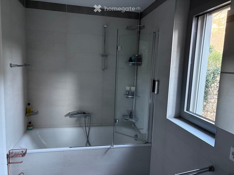 Bathroom with a bathtub, glass shower enclosure, shelves, and a window.