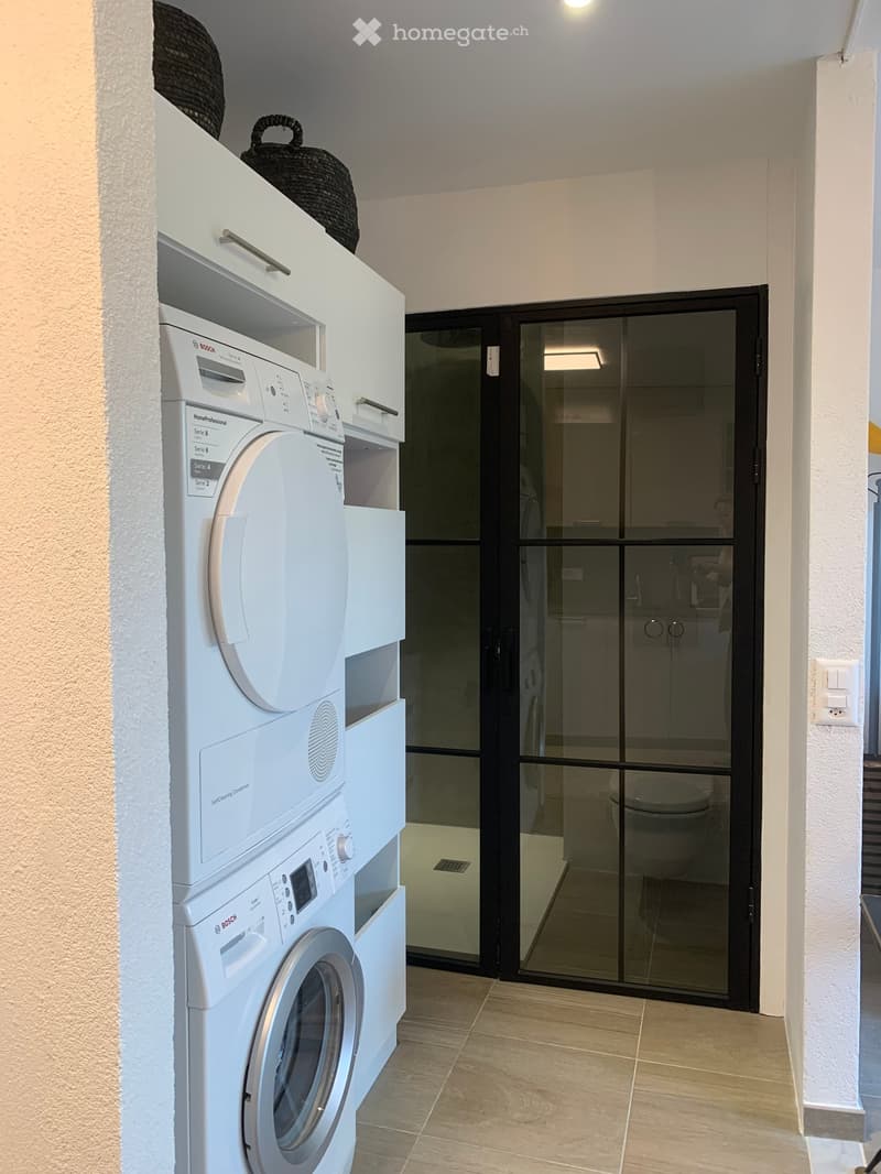 Laundry room with a white washing machine and dryer, tiled floor, glass door, and a power outlet on the wall