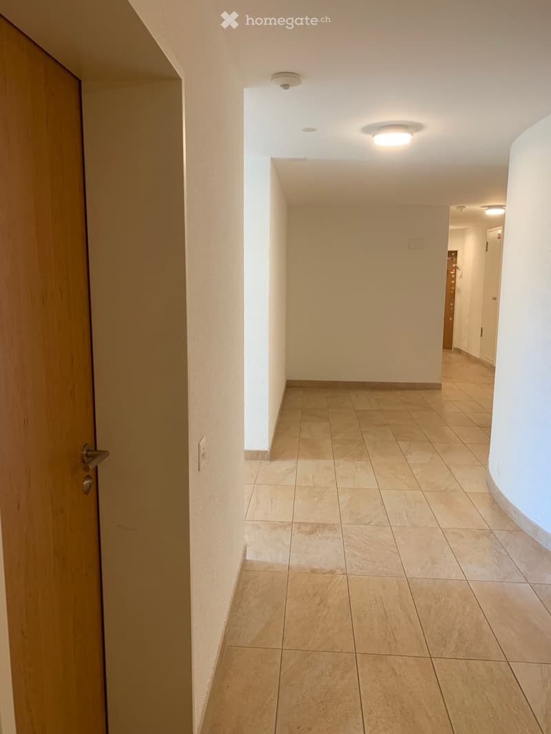 Empty hallway with tiled floor, white walls, and ceiling lights