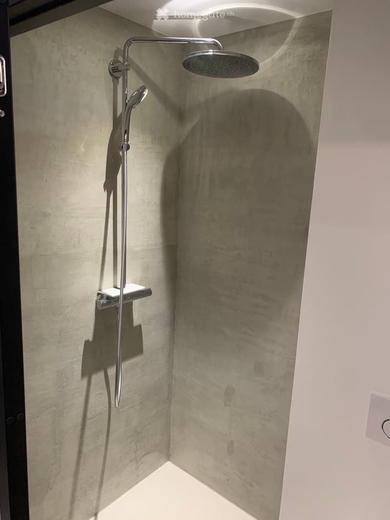 shower area with shower head and shower arm, concrete walls, white floor