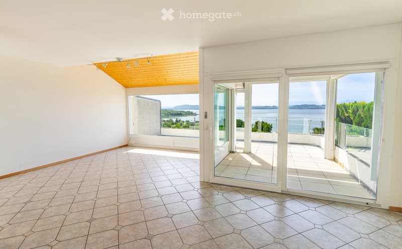 Empty room with white walls, hexagonal tiled floor, large glass sliding doors leading to a balcony with a scenic view of water and distant hills.