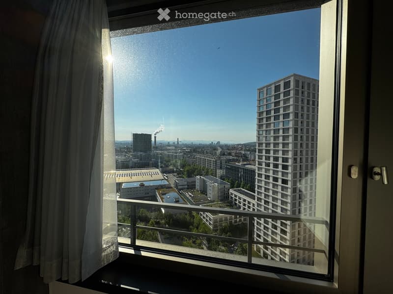 View from a balcony showing a cityscape with modern high-rise buildings, industrial structures, and a clear blue sky.