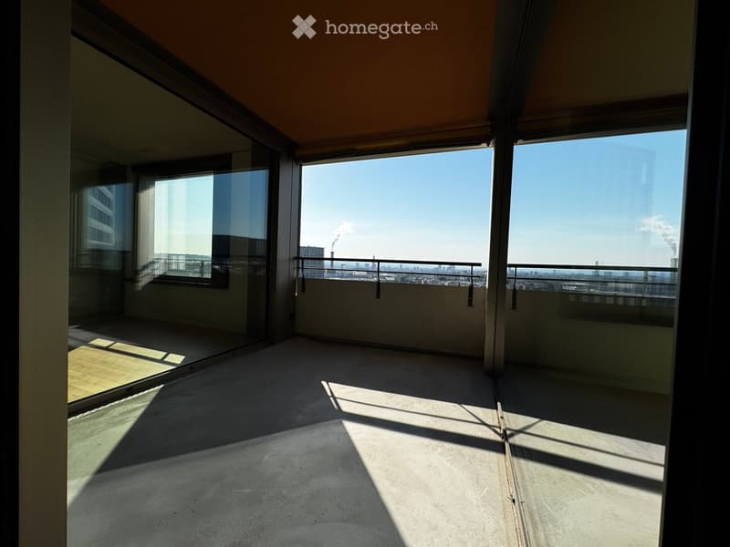 Empty balcony with large windows, metal railing, and a cityscape view.