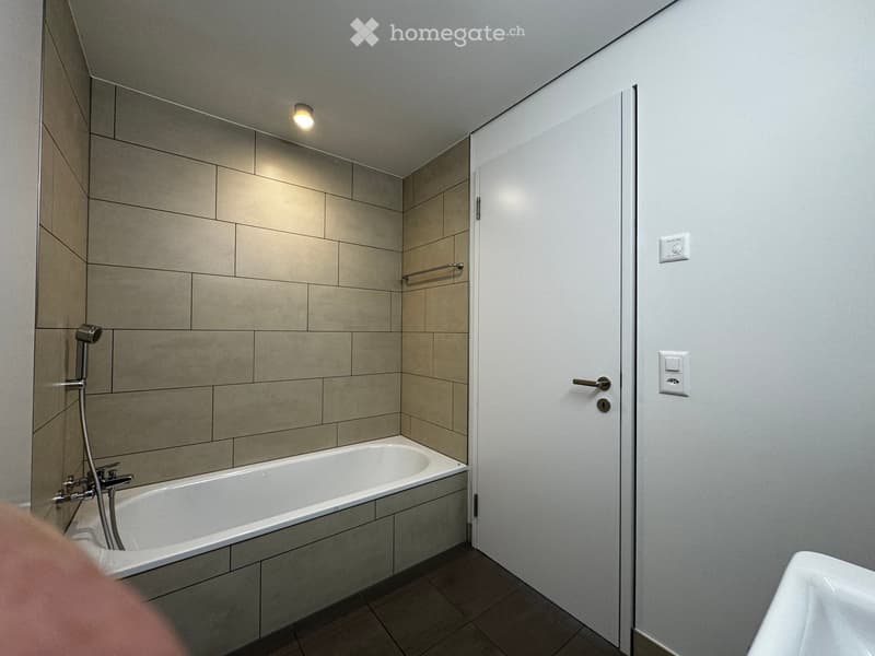 Modern bathroom with a bathtub, tiled walls, a showerhead, and a door.
