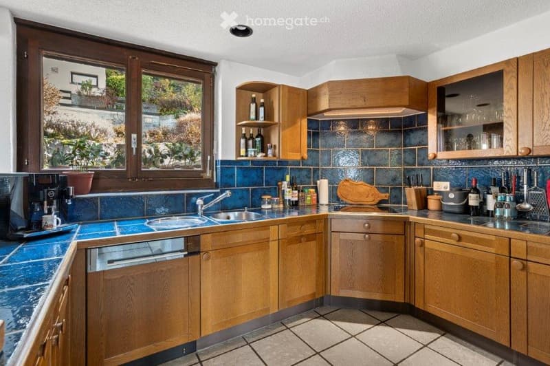 kitchen with wooden cabinets, blue tiles, sink, dishwasher, coffee machine, wine bottles, chopping board, knives, and a window with a view