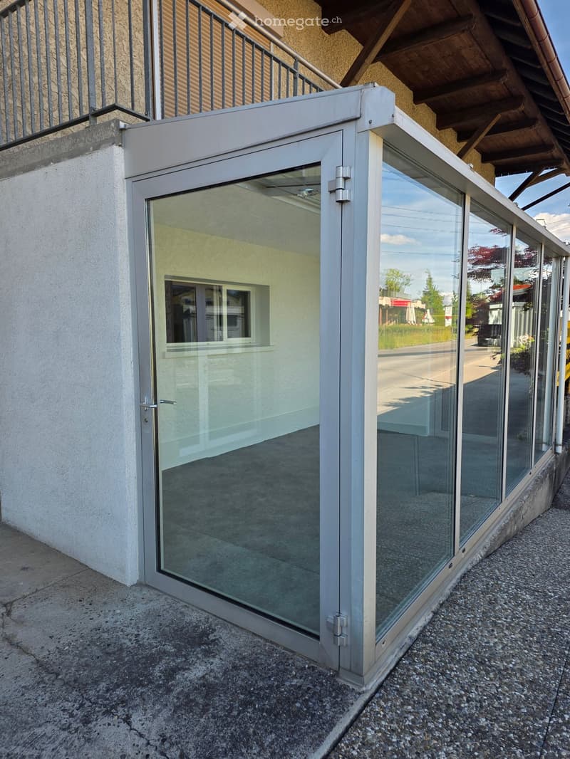 Modern glass balcony with sliding doors, white frame, and metal railing attached to a building.