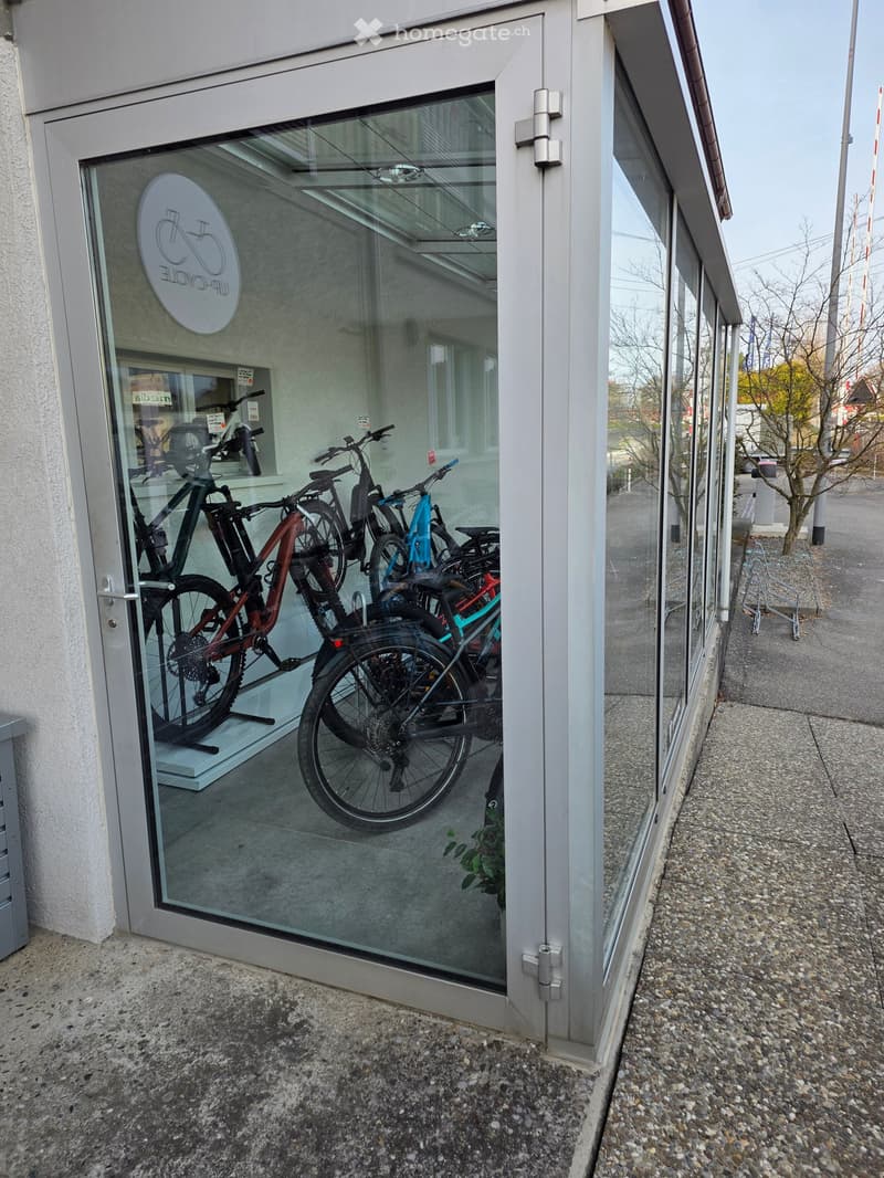 A glass door entrance to a building with bicycles displayed inside, a logo on the glass, and a reflection of the outside environment.
