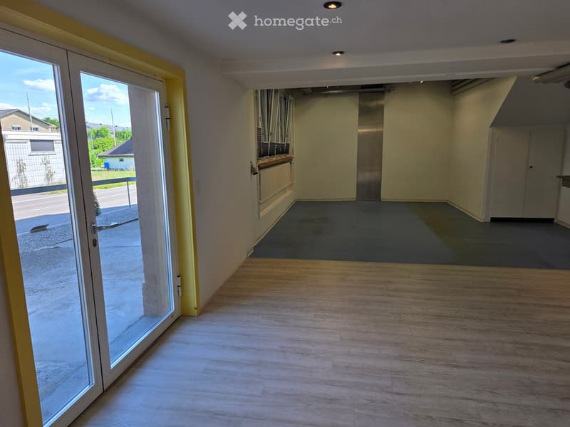 Empty room with wooden flooring, large sliding glass door leading outside, and a view of the street.