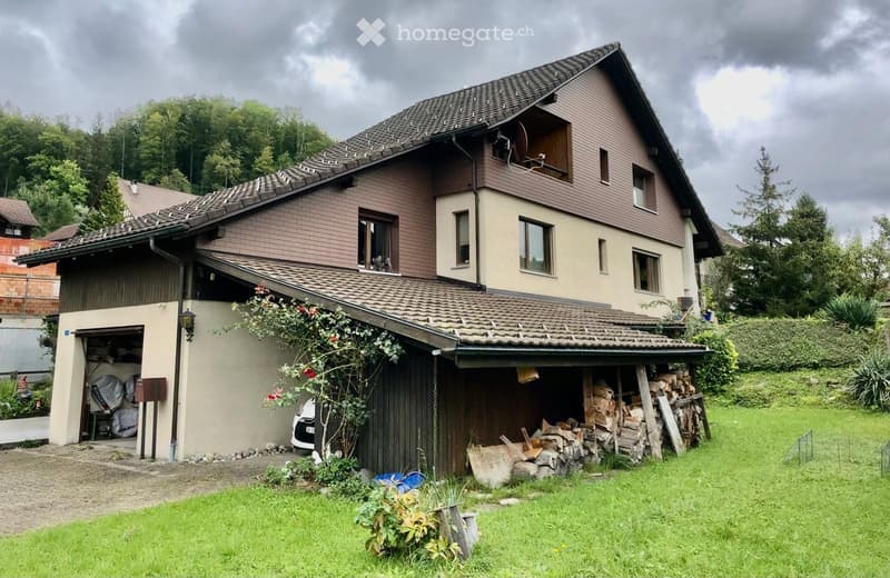 2 story house, brown exterior, garage, green lawn, trees in the background
