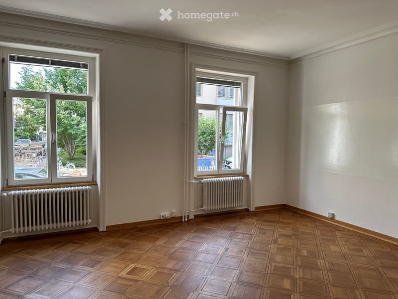 Empty room with wooden parquet flooring, white walls, and large windows with radiators beneath them.