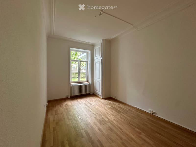 Empty room with wooden flooring, white walls, a window with a radiator below, and a white door.