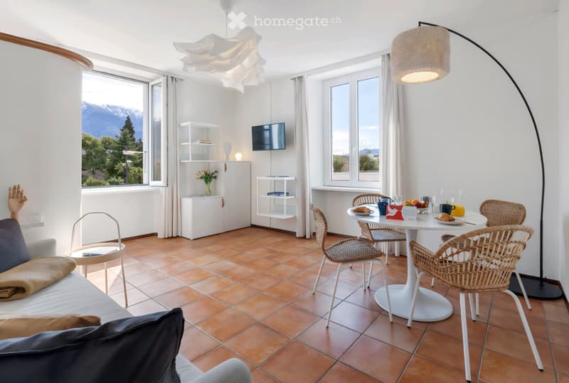 modern living room with white walls, brown tiles, white furniture, dining table, TV, windows, view of mountains