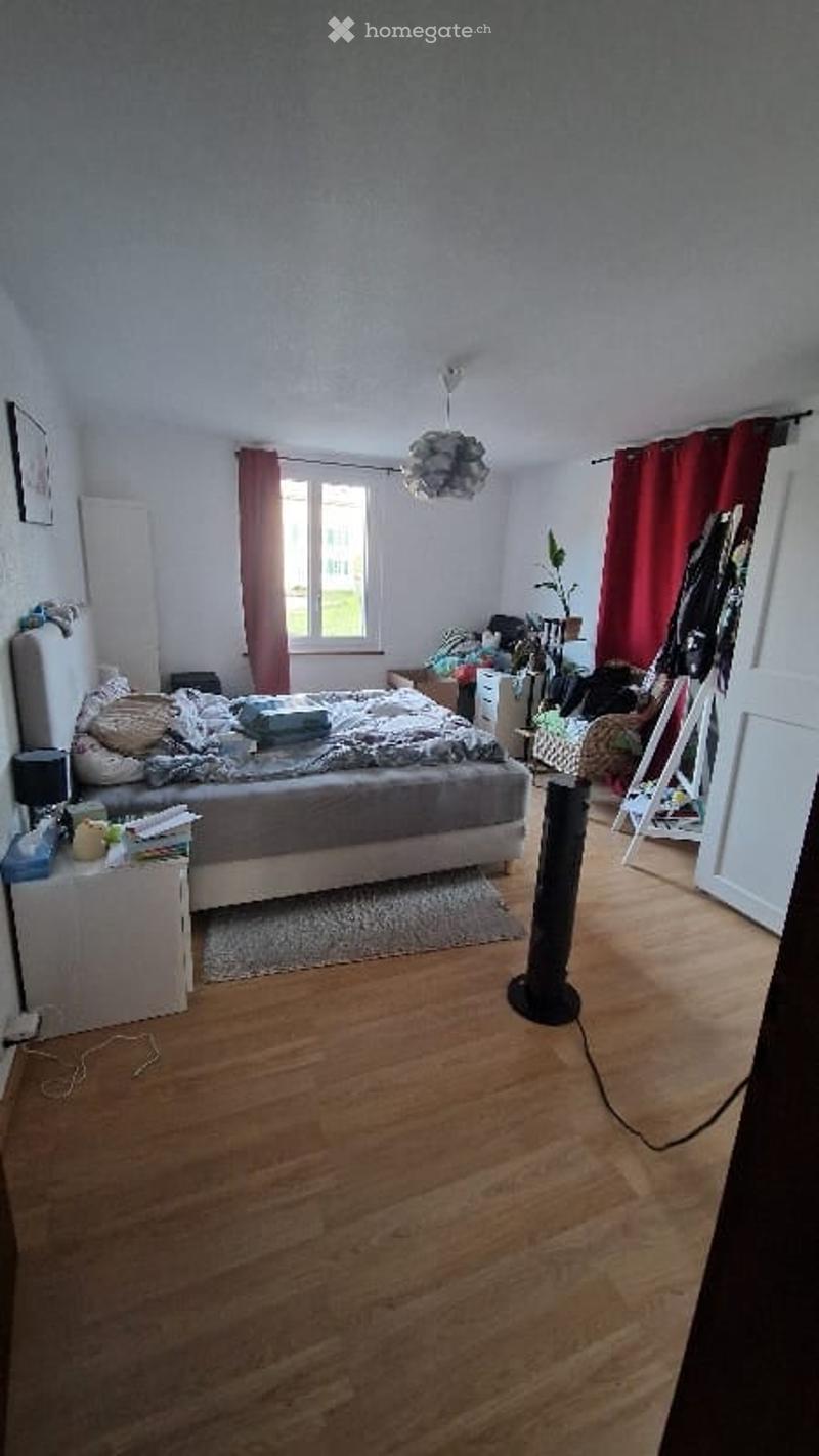 Bedroom with bed, nightstands, rug, fan, window with red curtains, picture frame, plant, storage boxes, and a lamp