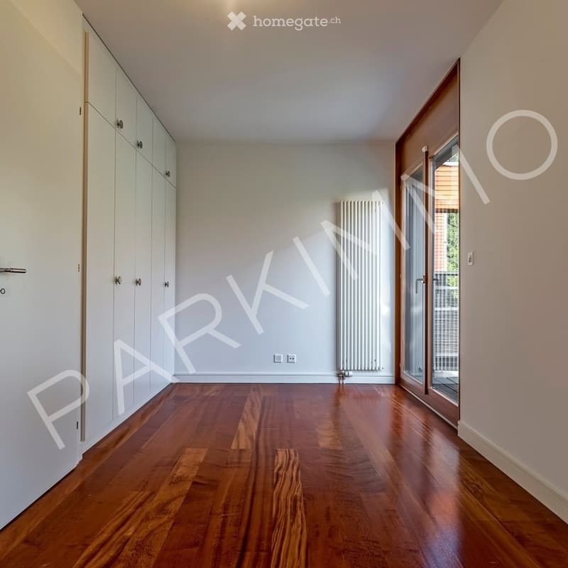 Empty room with wooden flooring, white walls, built-in wardrobes, and a radiator. No furniture or equipment present.