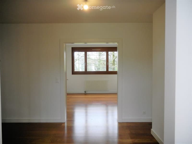Empty room with wooden floor, white walls, window with view to outside, white radiator