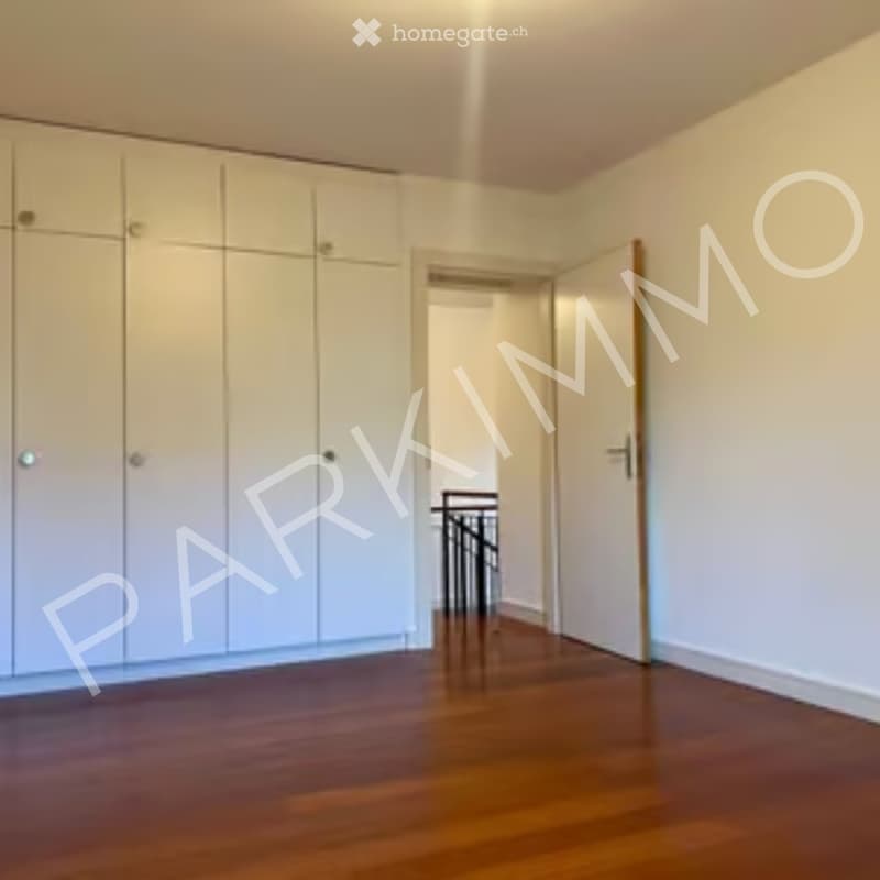 Empty room with wooden flooring, white walls, built-in wardrobes, and a doorway leading to another area.