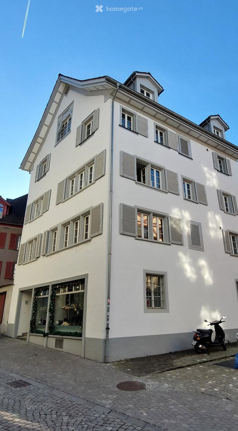 white building, multiple windows, grey shutters, ground floor shop, cobblestone street