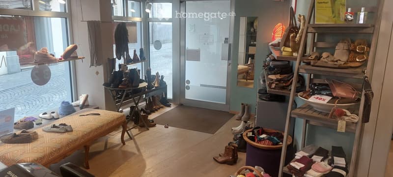 Shop with wooden floor, shelves with shoes, bags, and accessories, a bench, and a mirror.