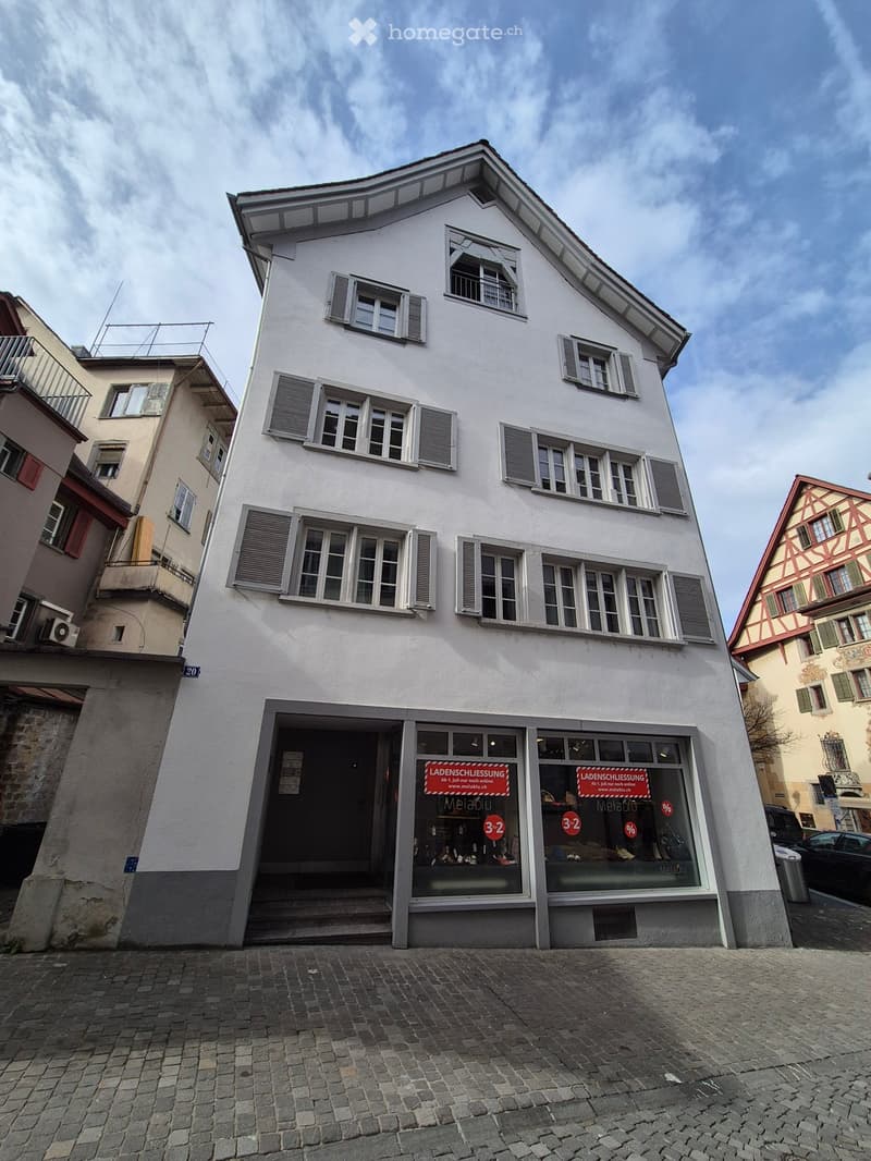 White building with multiple windows, red sign with text 'Ladenschlussung', number '3-2', and percentage sign