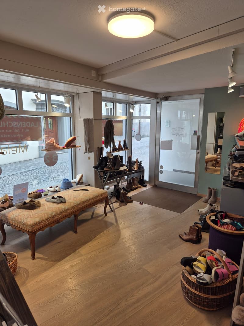 shoe store with wooden floor, large windows, hanging lamps, bench, baskets of shoes, shoe rack, mirror