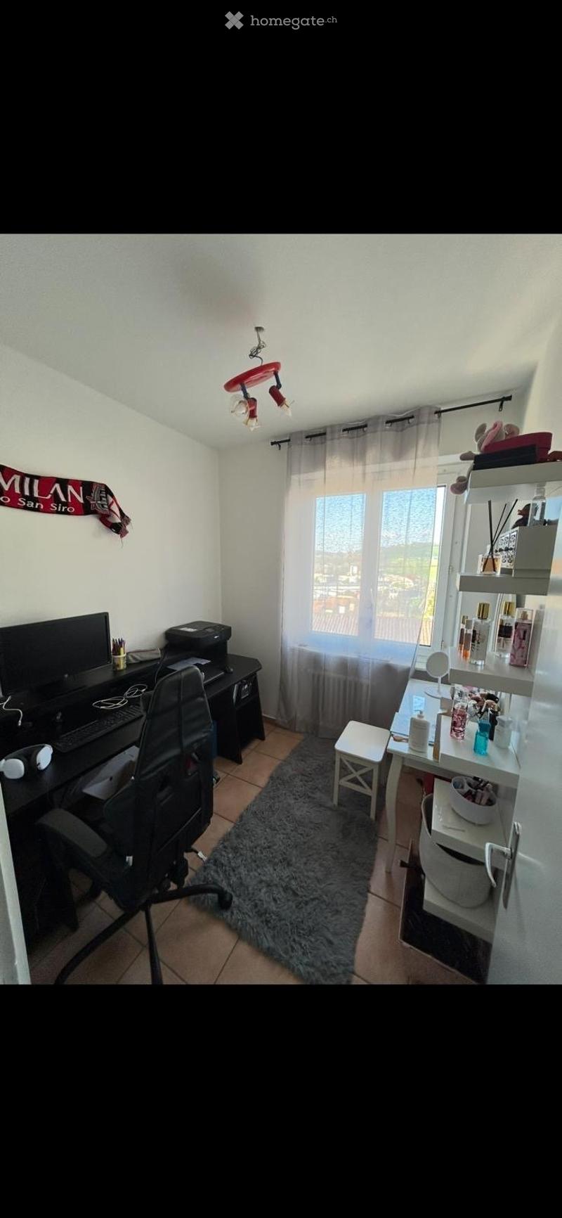 A room with a desk, chair, monitor, keyboard, mouse, printer, rug, shelves, stool, and window with curtains.