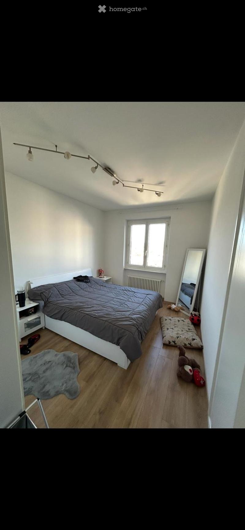 Bedroom with bed, nightstand, radiator, mirror, toys, rug, wooden floor, window, track lighting