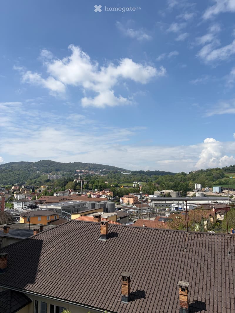Aerial view of a town with many buildings, mountains in the background, and a clear blue sky with clouds.