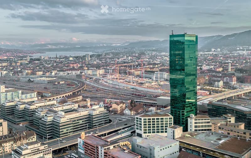 Aerial view of a city with many buildings, a prominent green skyscraper, and a highway with multiple lanes.