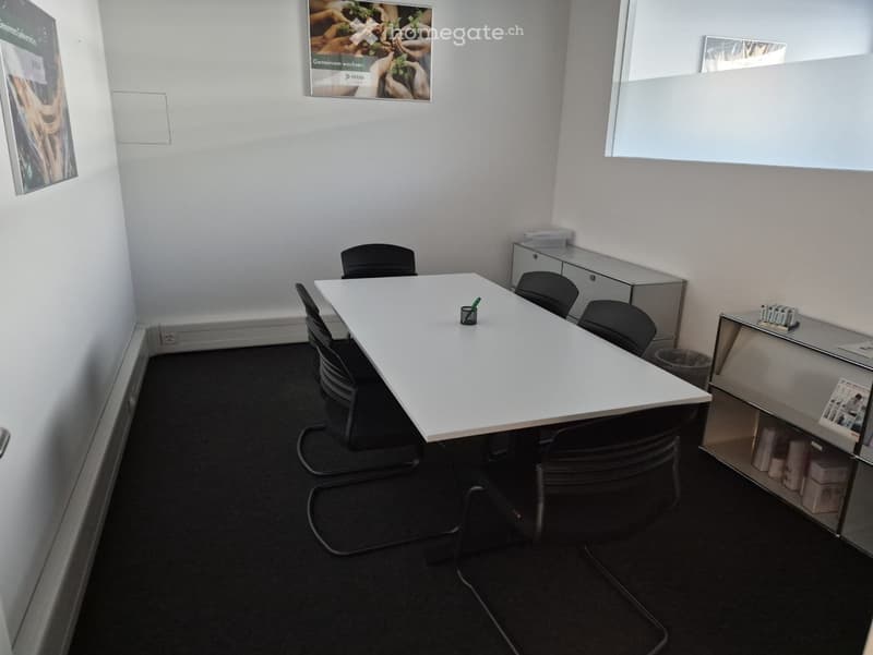empty meeting room with white table, black chairs, white walls, posters, trash bin, cabinet
