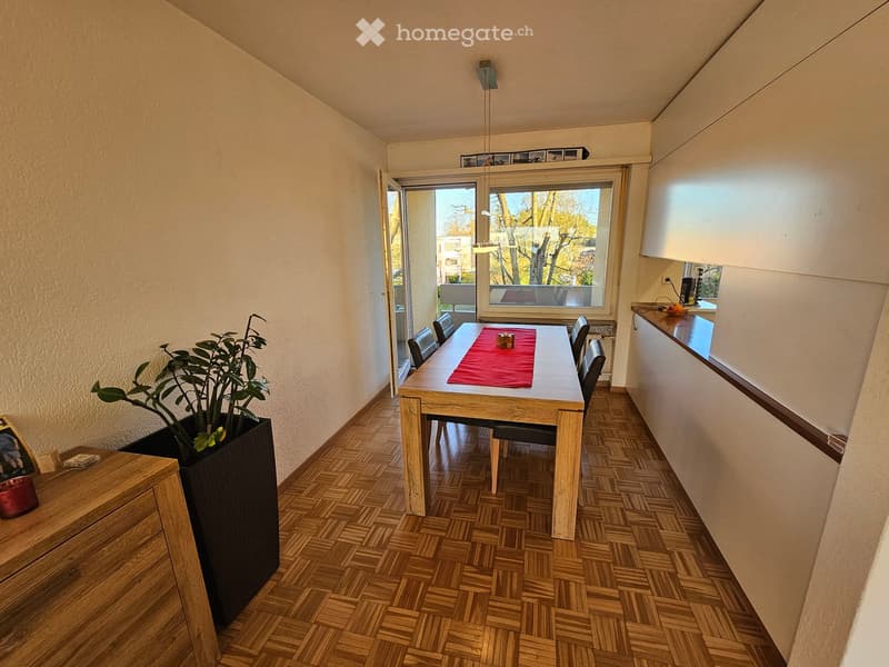 Dining room with wooden floor, dining table, chairs, potted plant, sliding glass door, balcony, kitchen area, wooden cabinet, picture frame, candle