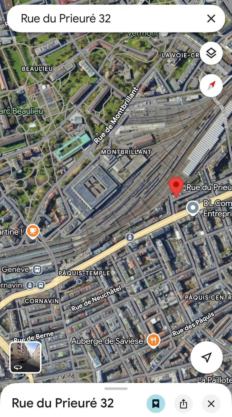 Aerial view of a city with various streets, buildings, and landmarks. The map shows Rue du Prieuré 32, a street with a red marker indicating a specific location. Other streets include Rue de Neuchâtel, Rue de Montbrillant, and Rue des Paquis. There are al