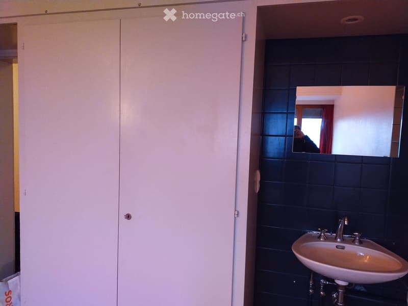 A bathroom with a white sink, mirror, and blue tiles on the wall. There is a white cabinet with two doors.