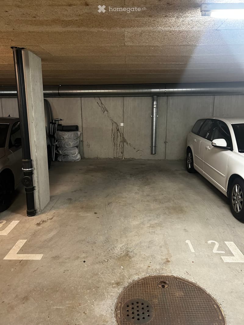 underground parking lot, concrete floor, two cars parked, one car in the corner, pipes on the wall, manhole cover