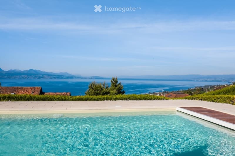 Outdoor swimming pool, wooden deck, manicured lawn, hedges, distant houses, mountains, and sea