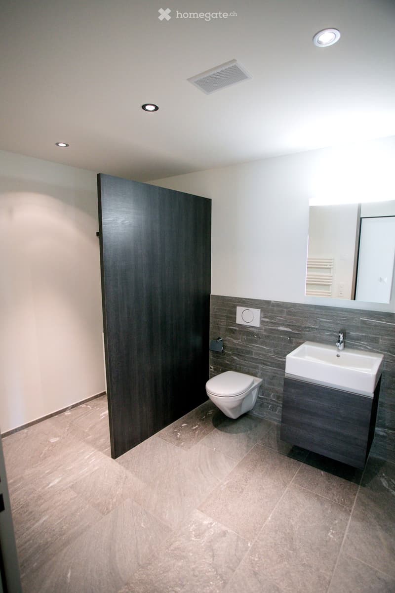 modern bathroom with white toilet, sink, mirror, and gray tiles