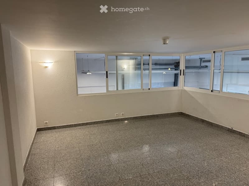 Empty room with white walls, tiled floor, large windows, and ceiling-mounted lamps.