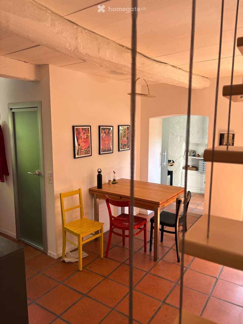 Dining area with wooden table, chairs, and framed pictures on the wall, tiled floor, and a door leading to another room