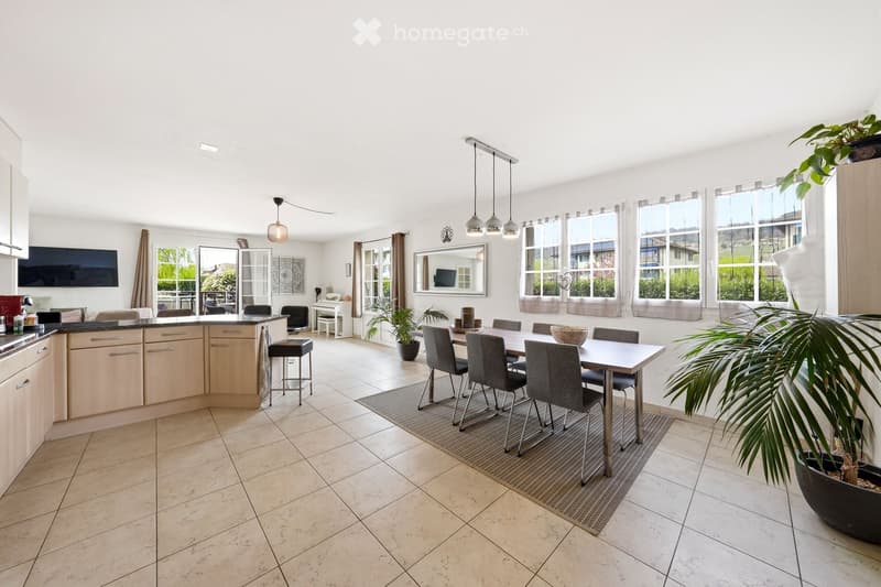Open plan kitchen and dining area, large windows, dining table, kitchen island, TV, plants