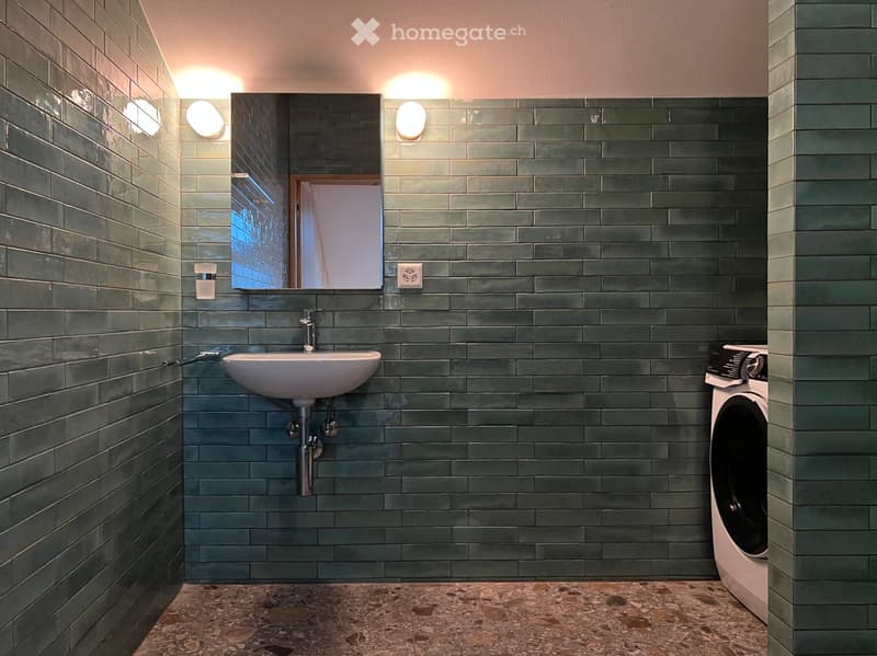 small bathroom with green tiles, white sink, mirror, washing machine