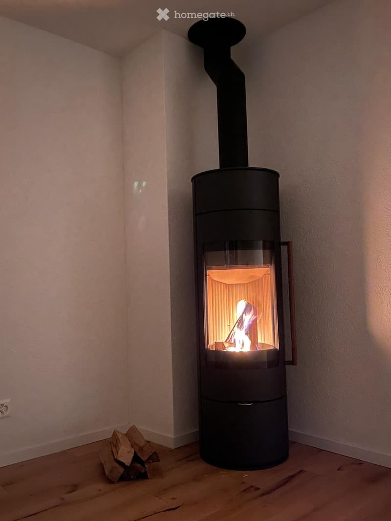 White walls, hardwood floors, black fireplace, wood pile