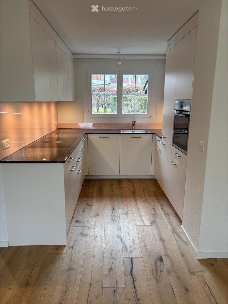 modern kitchen with white cabinetry, black countertop, wooden floor, white walls, stainless steel sink and faucet, integrated oven and microwave, large windows