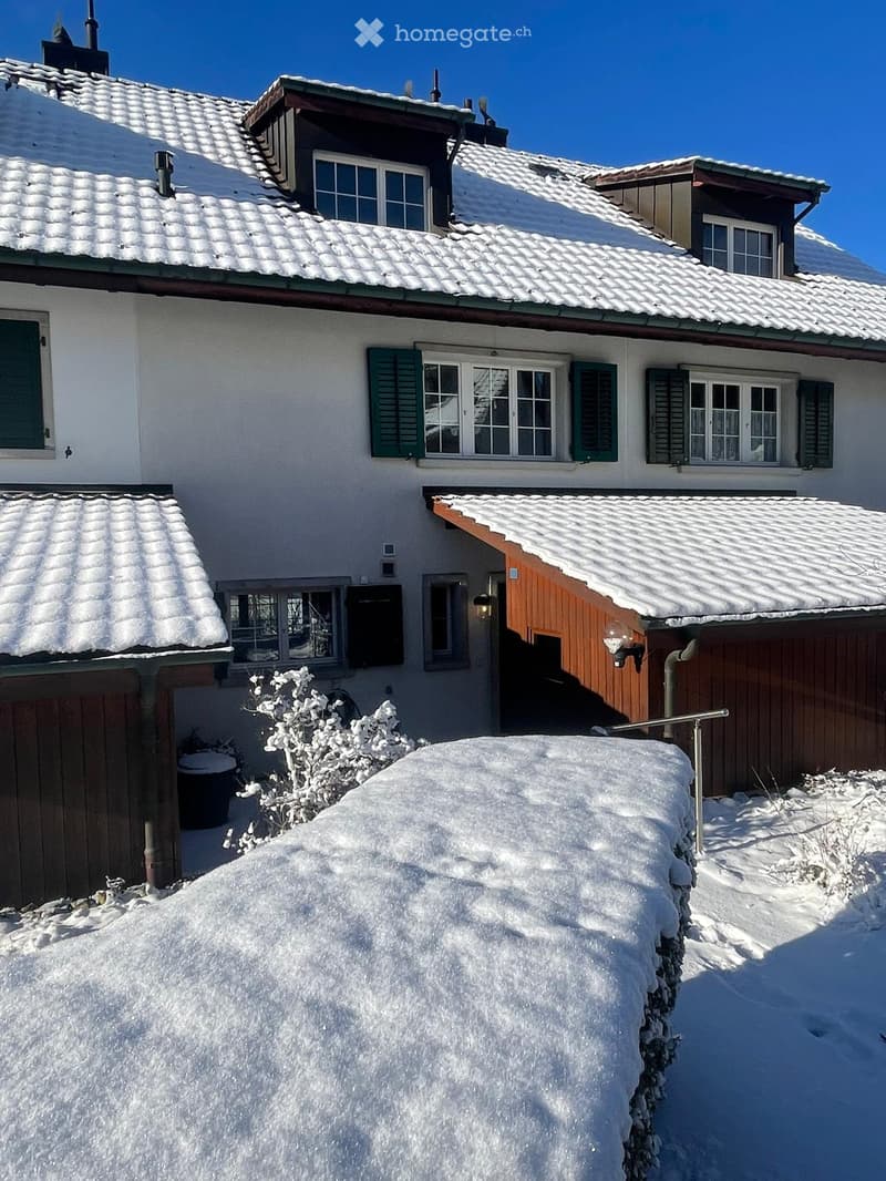 white two-storey house, wooden roof, brown shutters, covered entrance, garage with covered porch, covered with snow