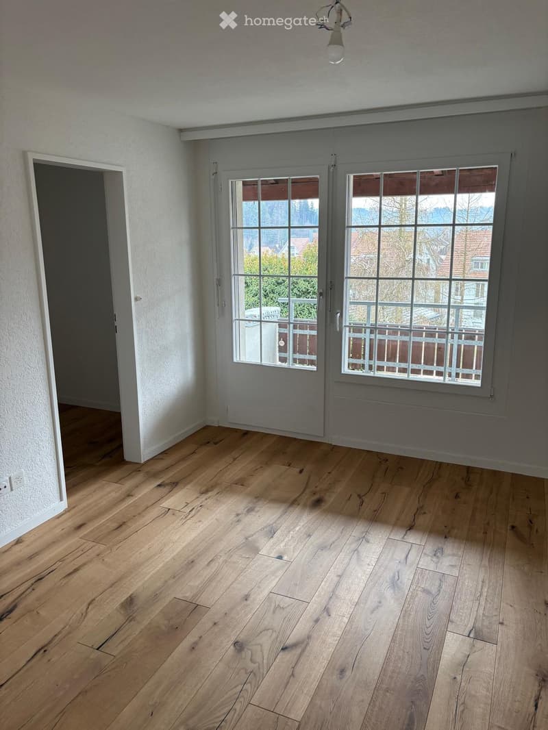 Empty room, wooden floor, white walls, double glass doors with balcony, large windows, power outlet