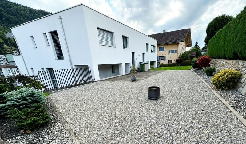 Modern white house, gravel driveway, black gate, small garden, mountain view