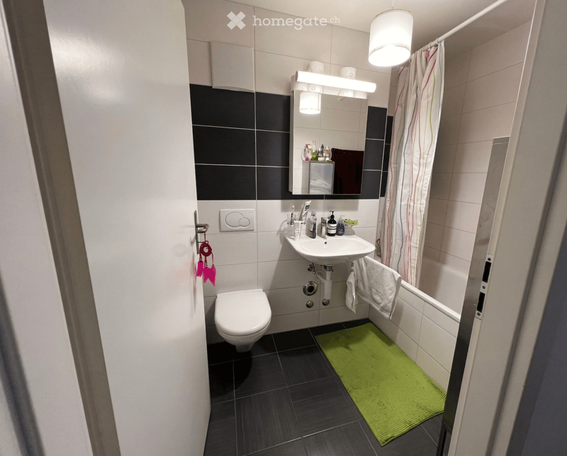Bathroom with toilet, sink, bathtub, mirror, shower curtain, green rug, white tiles, and black tiles